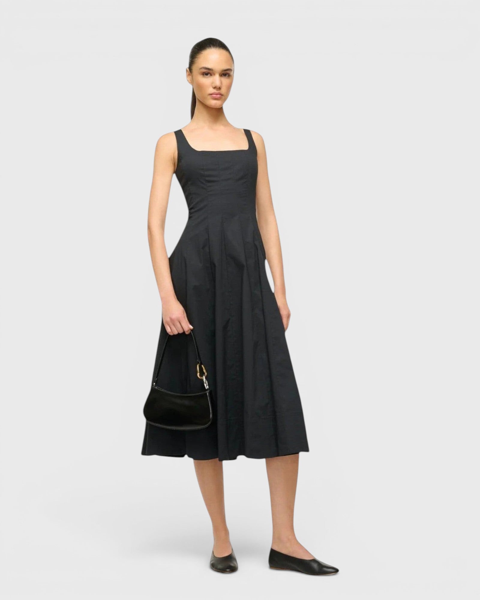 Model wearing a black midi dress and holding a JONES + CO Ollie Bag, a compact black leather shoulder bag.