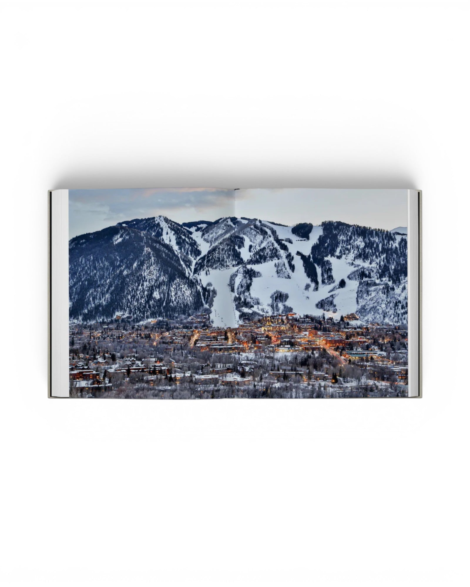 JONES + CO Private Aspen book open to a panoramic photograph of the snowy Aspen mountain landscape at twilight.