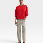 Model wearing a red JONES + CO Fond crewneck sweatshirt with drop shoulders and raw edge hem, paired with beige pants.