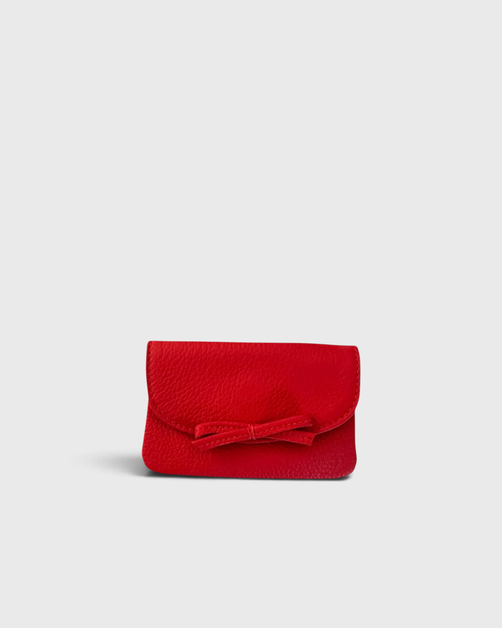 JONES + CO red leather petite case featuring a front flap with a decorative knotted bow and magnetic closure.