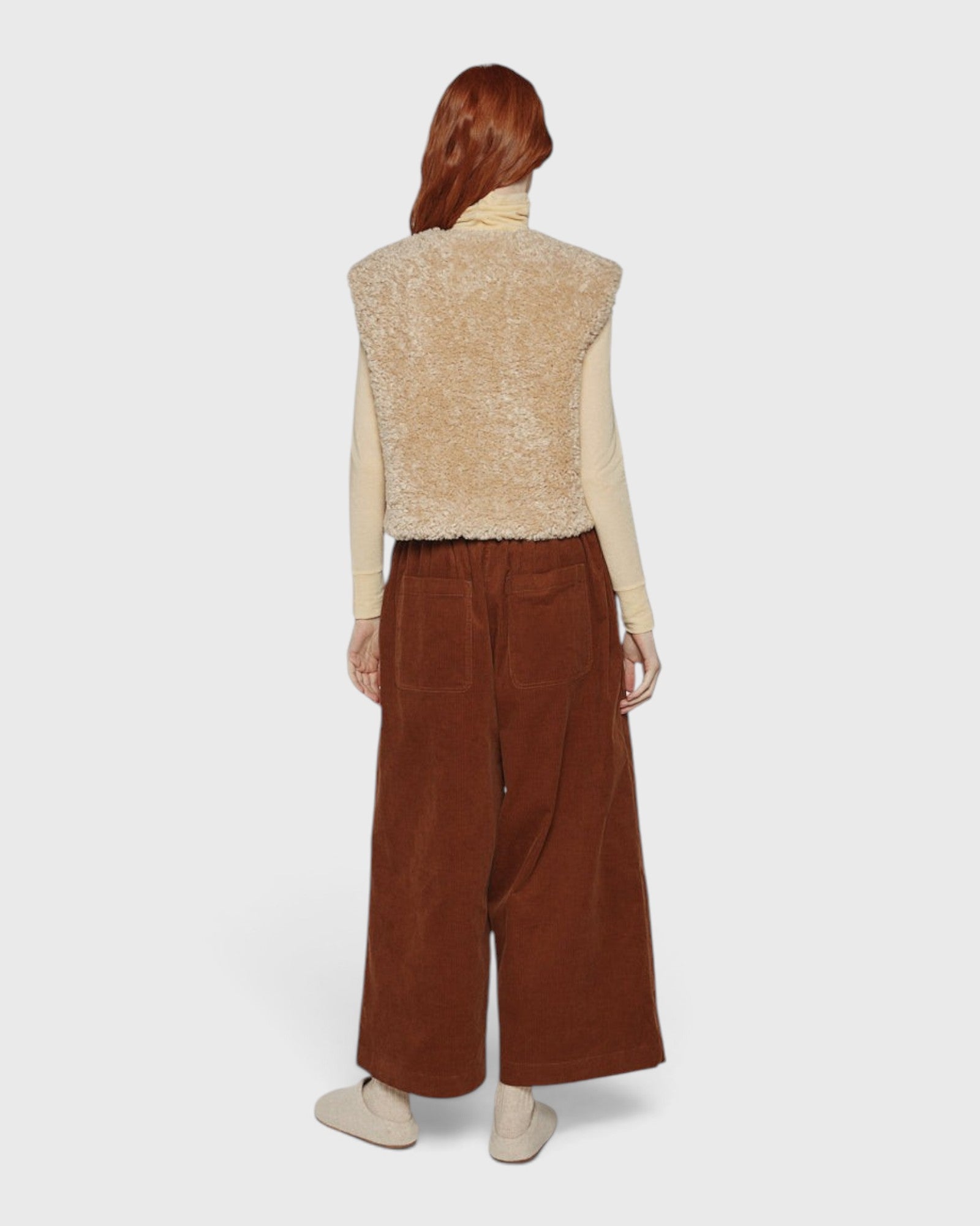 JONES + CO reversible oatmeal beige faux fur short vest worn over a cream turtleneck and brown corduroy trousers