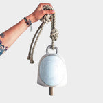 JONES + CO round stoneware bell in full moon white with a wood knocker and hemp rope held by a hand