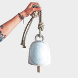 JONES + CO round stoneware bell in full moon white with a wood knocker and hemp rope held by a hand
