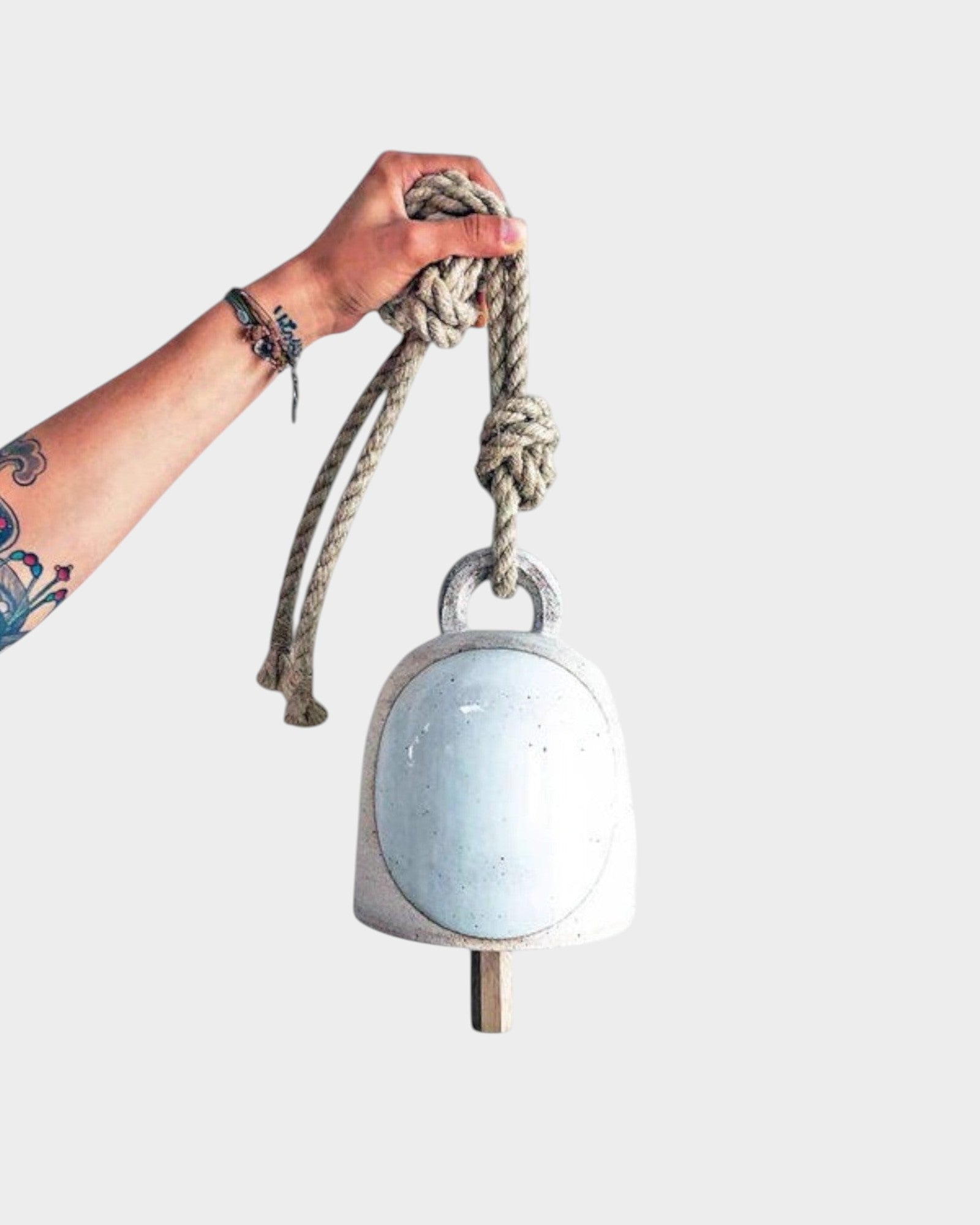 JONES + CO round stoneware bell in full moon white with a wood knocker and hemp rope held by a hand