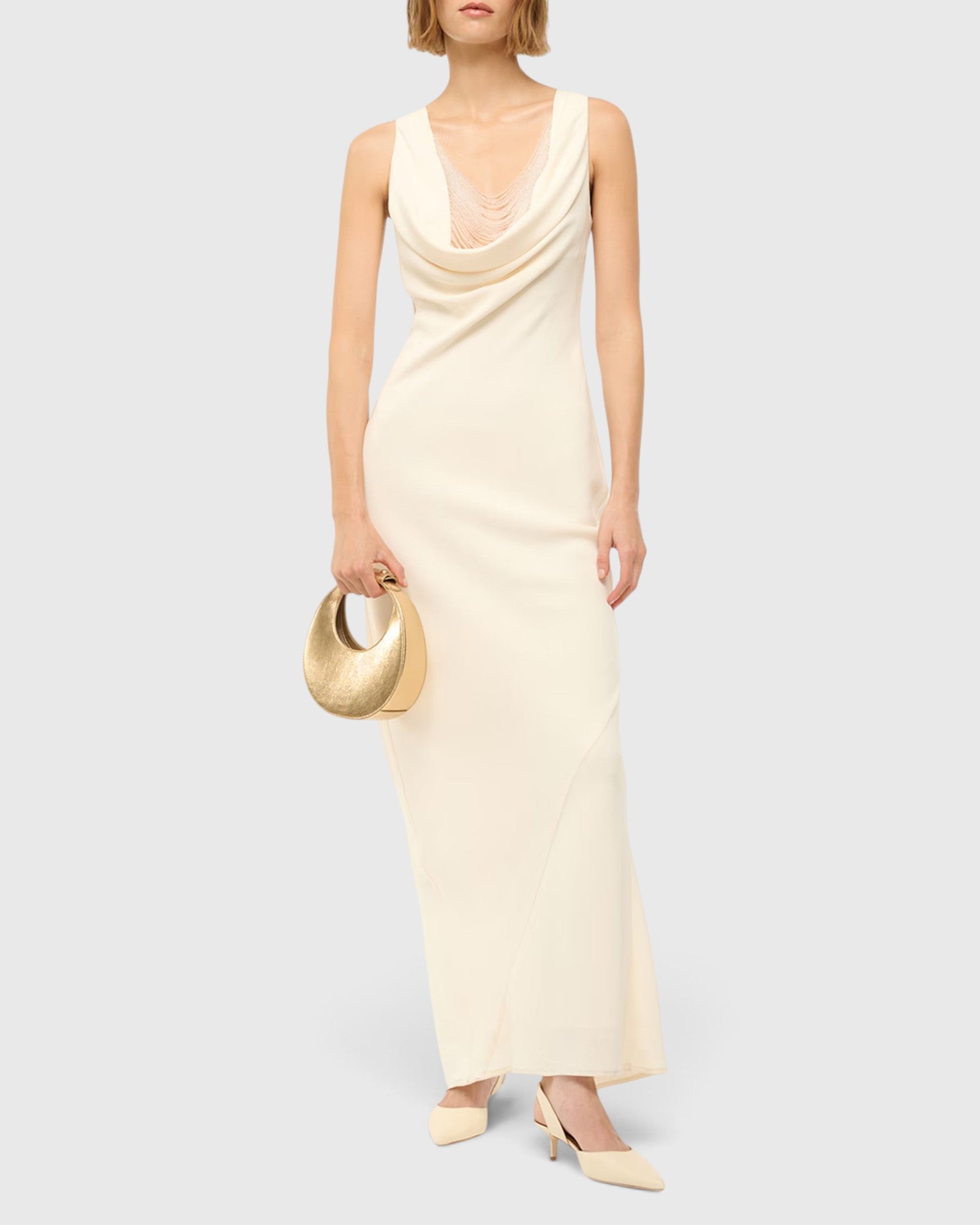 JONES + CO STAUD Good Night Moon evening bag in polished gold held by a model in a cream cowl-neck maxi dress