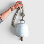 JONES + CO round stoneware bell in full moon white with a wood knocker and hemp rope held by a tattooed hand