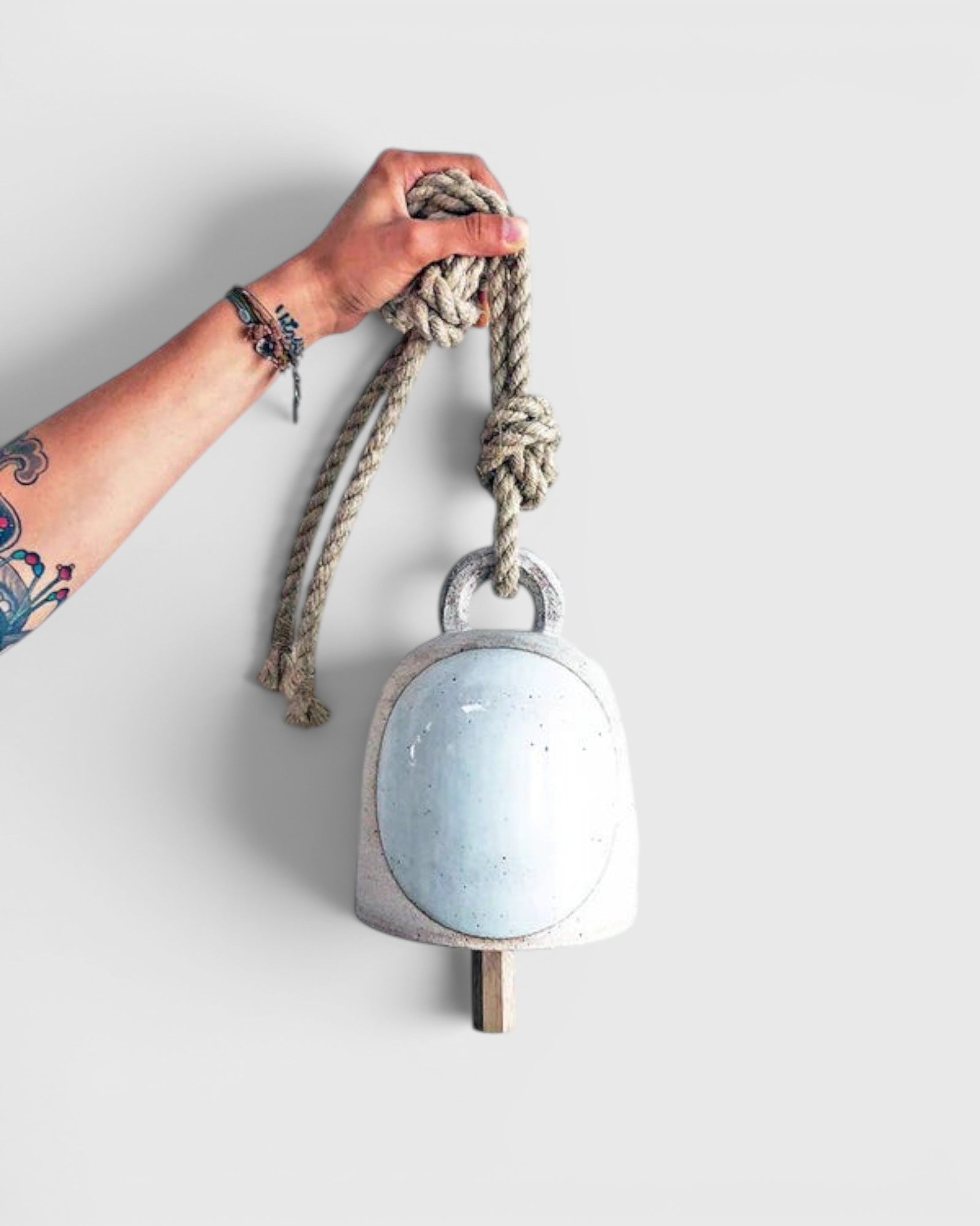 JONES + CO round stoneware bell in full moon white with a wood knocker and hemp rope held by a tattooed hand