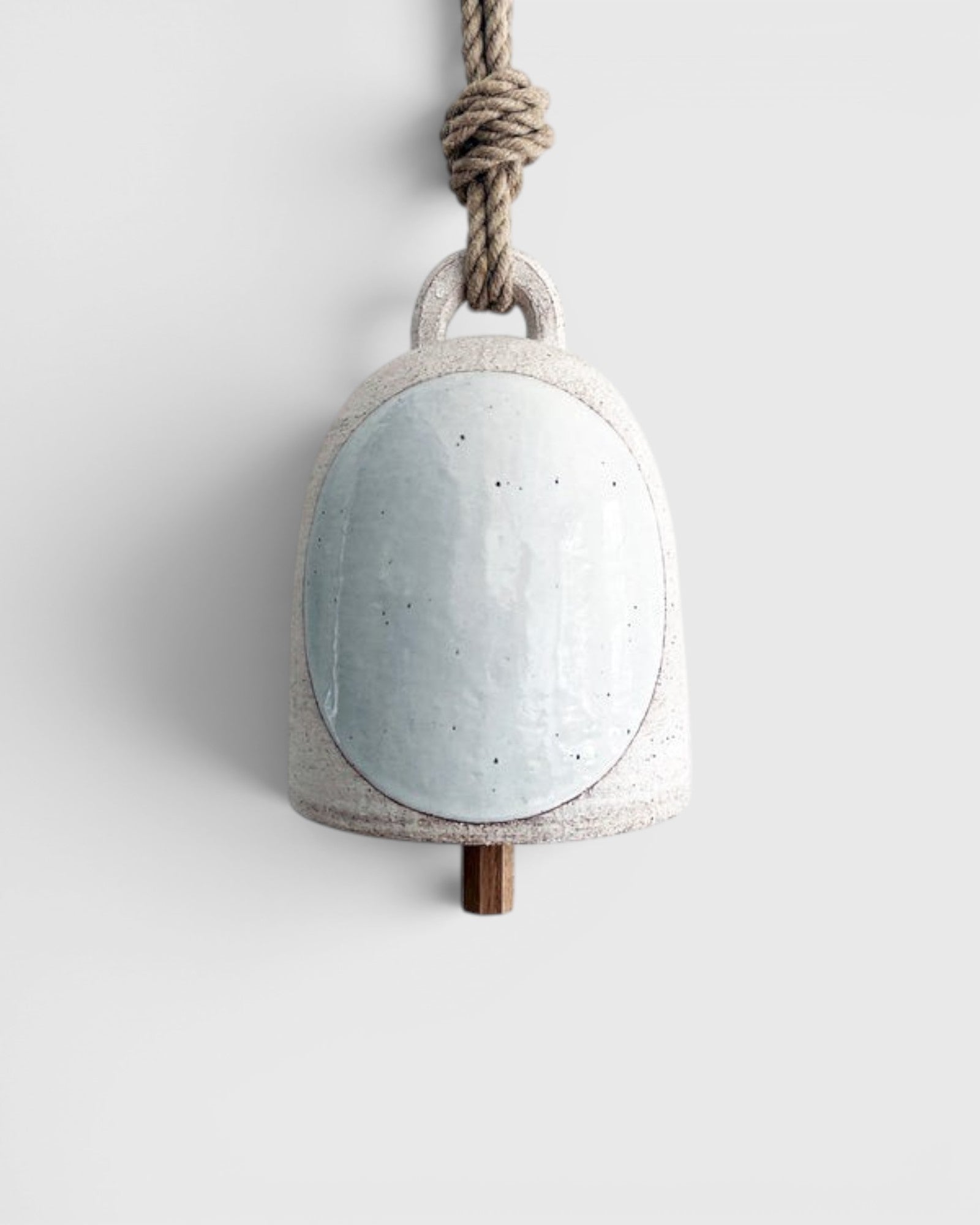 JONES + CO small round stoneware bell in white with a glazed full moon design, wood knocker, and hemp rope hanger.