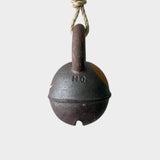 JONES + CO round extra dark stoneware jingle bell with yellow crescent detail hanging on a rustic hemp rope.