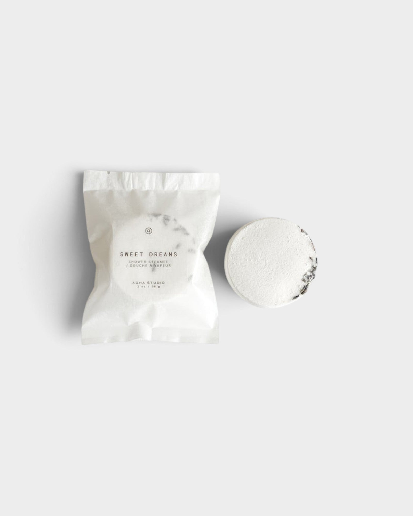 JONES + CO Sweet Dreams shower steamer in white packaging next to a single round lavender and vanilla scented tablet.