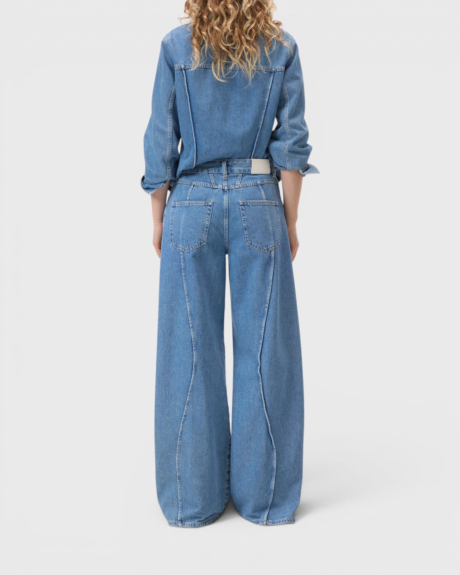 JONES + CO Tali-X wide-leg denim jeans in mid blue with curved seaming and high waist, back view on a model.