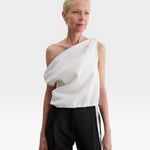 Model wearing a white JONES + CO Farfalla one-shoulder top in Italian Foam fabric with draped, gathered shoulder detail.