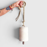 JONES + CO tall white stoneware bell with a star detail, wooden knocker, and hemp rope held by a tattooed hand.