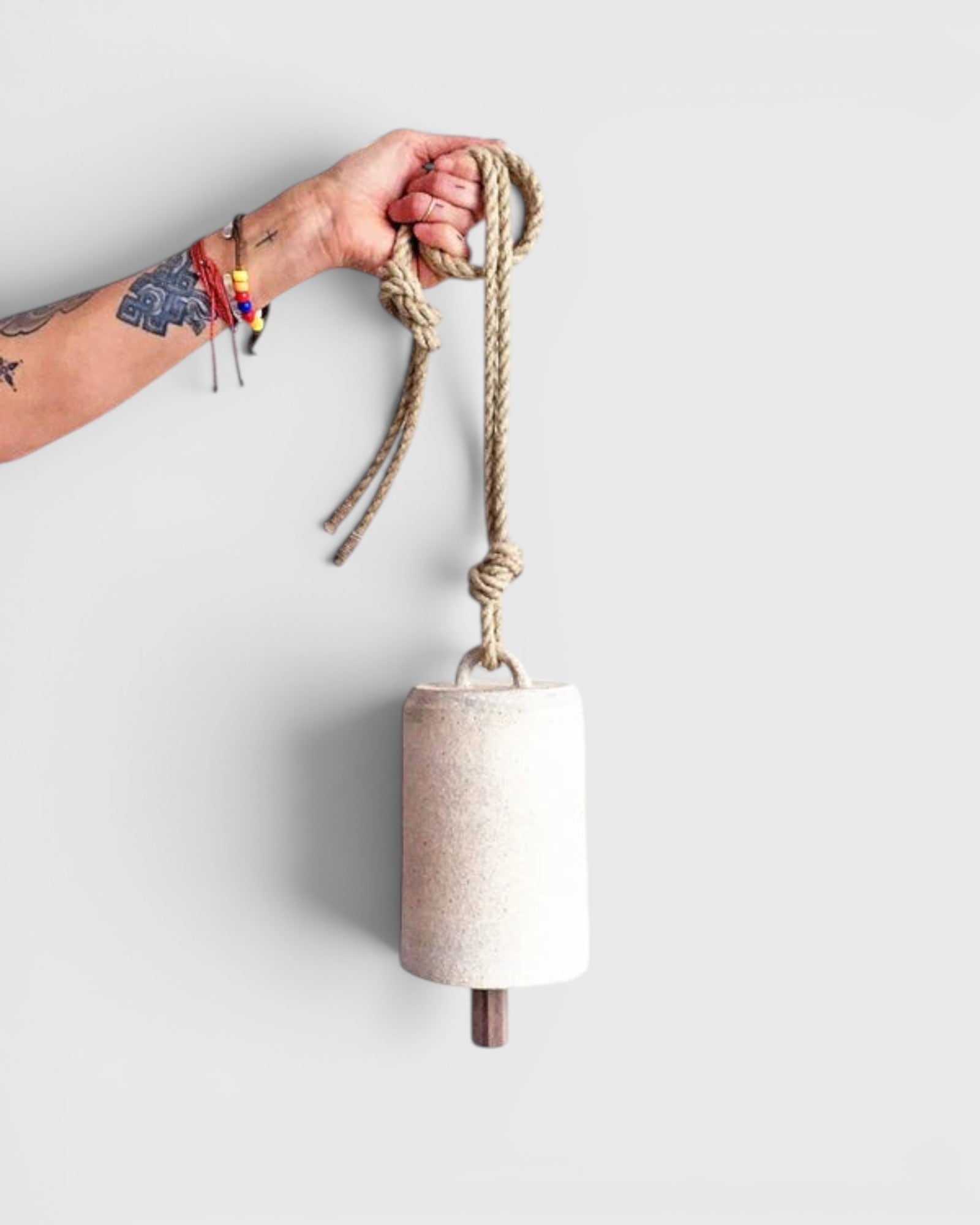 JONES + CO tall white stoneware bell with a star detail, wooden knocker, and hemp rope held by a tattooed hand.