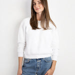 Model wearing a white JONES + CO Ziggy sweatshirt with cropped sleeves paired with blue denim jeans