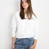 Model wearing a white JONES + CO Ziggy sweatshirt with cropped sleeves paired with blue denim jeans