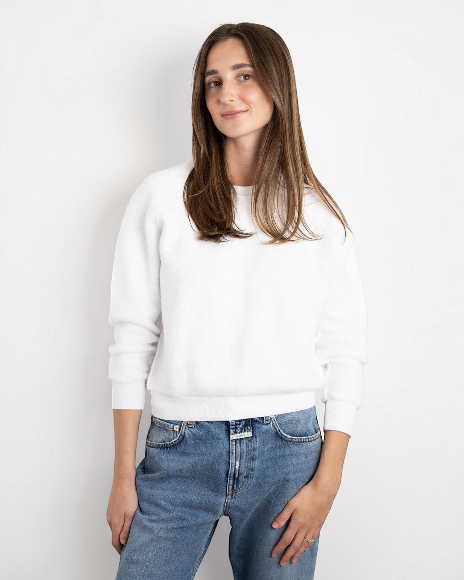 Model wearing a white JONES + CO Ziggy sweatshirt with cropped sleeves paired with blue denim jeans