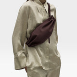 JONES + CO Bon-Bon M wine leather crossbody bag with pleated ends and brass hardware worn by a model