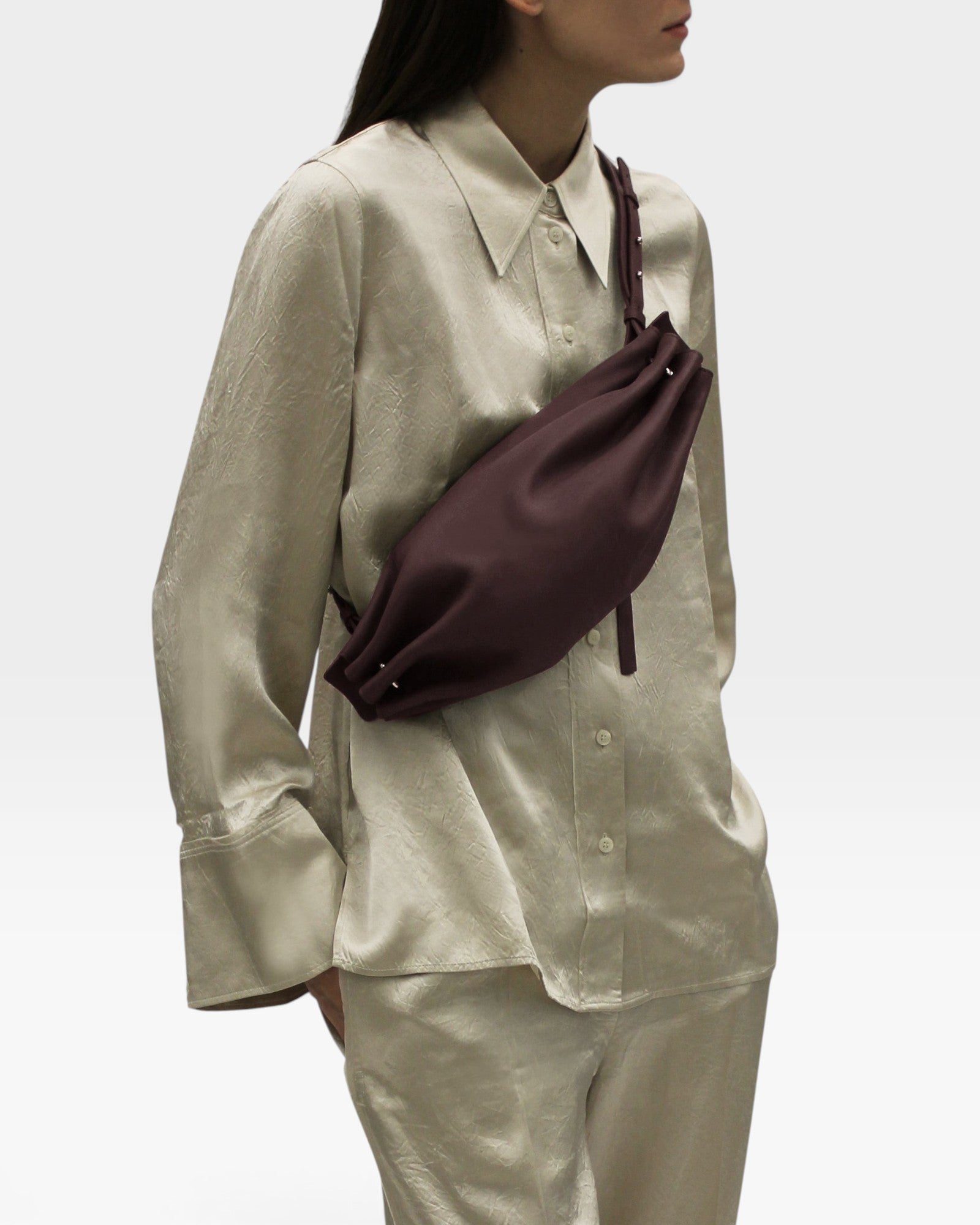 JONES + CO Bon-Bon M wine leather crossbody bag with pleated ends and brass hardware worn by a model