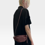 JONES + CO Bon-Bon wine-colored calf leather shoulder bag with pleated ends and palladium hardware worn by a model.