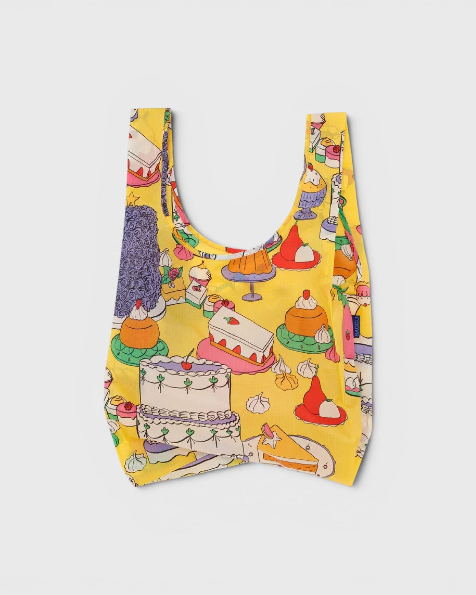 JONES + CO Baggu reusable grocery bag in yellow ripstop nylon featuring a colorful patisserie cake print