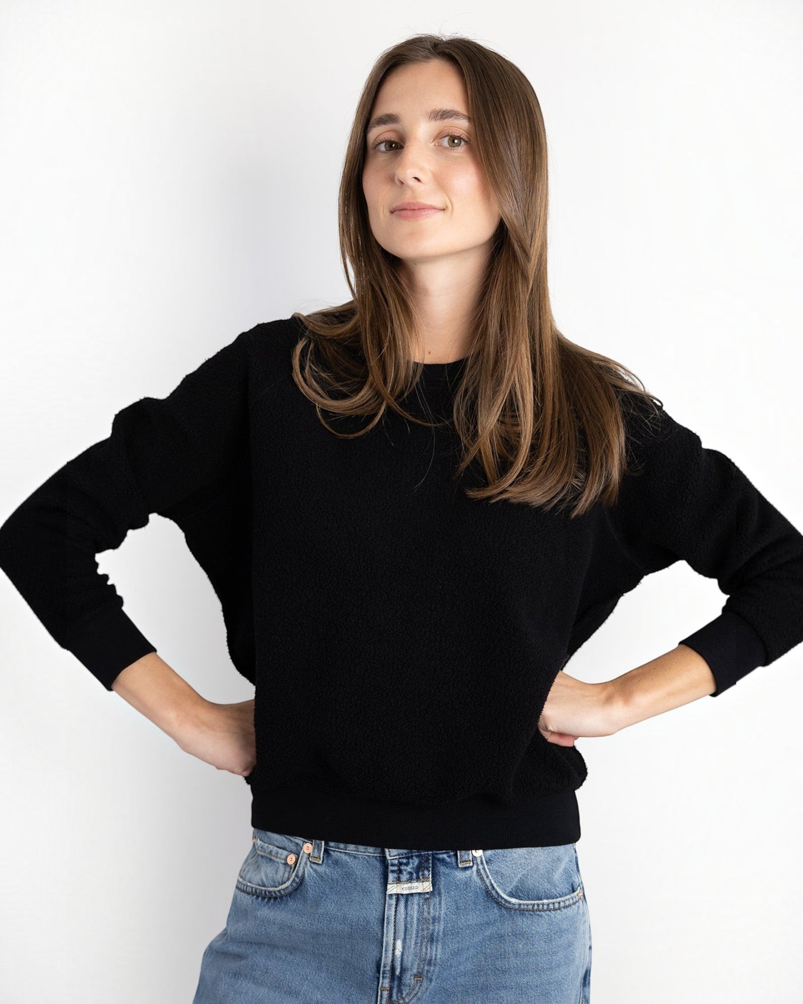 Model wearing a JONES + CO black Ziggy sweatshirt with a shrunken fit and cropped sleeves, paired with blue jeans.