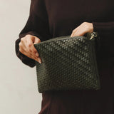 Person holding a woven green clutch bag against a plain background