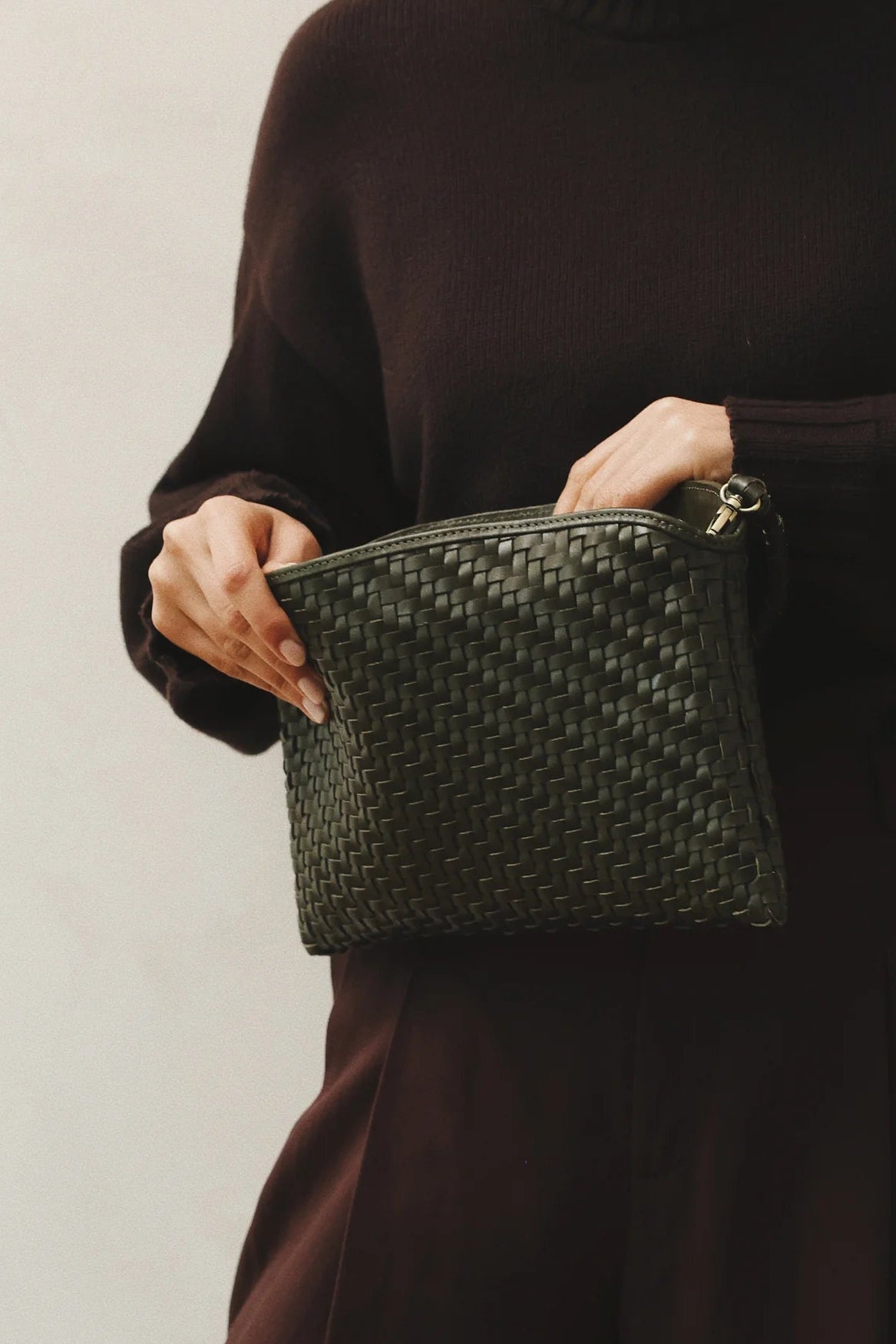 Person holding a woven green clutch bag against a plain background