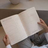 Person holding a notebook titled 'Reflections' with a candle and vase in the background.