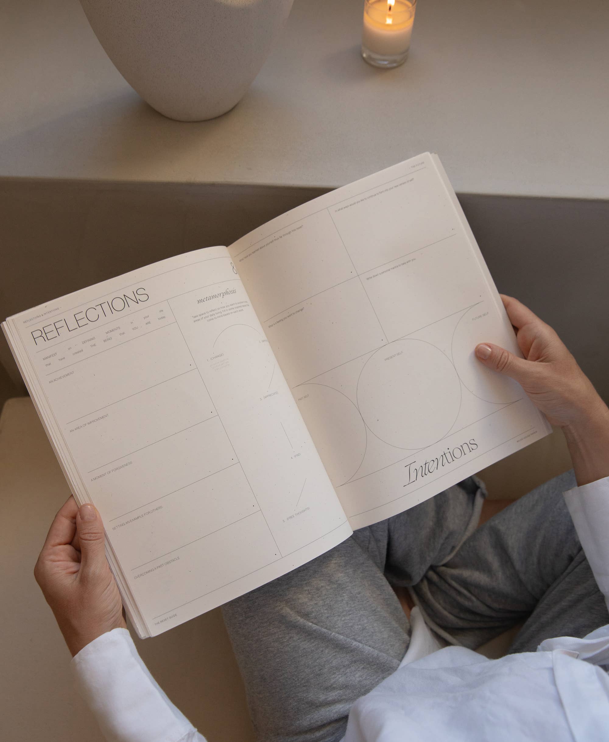 Person holding a notebook titled 'Reflections' with a candle and vase in the background.