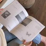 Person reading an open book with butterfly illustrations on a wooden floor.