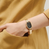 Gold watch on a wrist with a mustard yellow garment