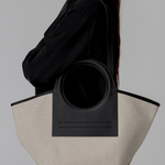 Person holding a black and beige tote bag against a gray background