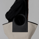 Person holding a black and beige tote bag against a gray background