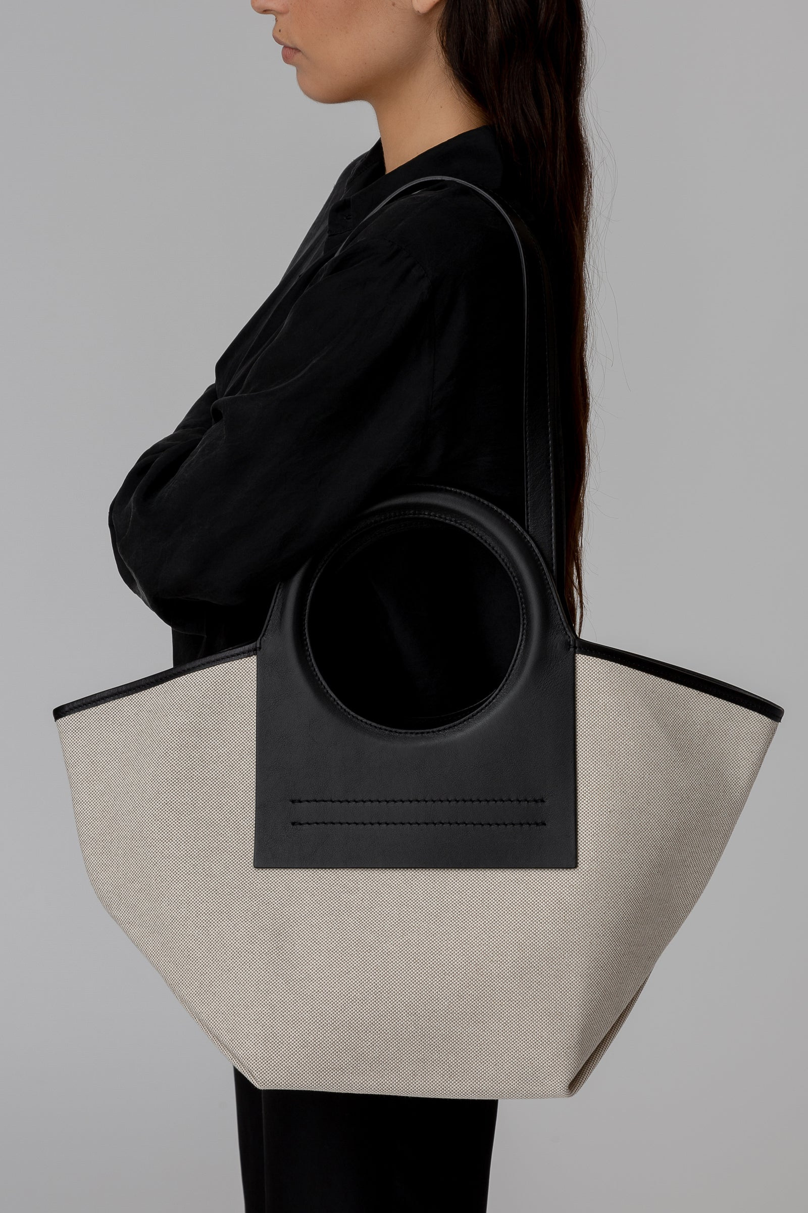 Person holding a black and beige tote bag against a gray background