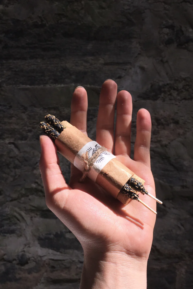 Hand holding two lit cigarettes against a dark stone wall background