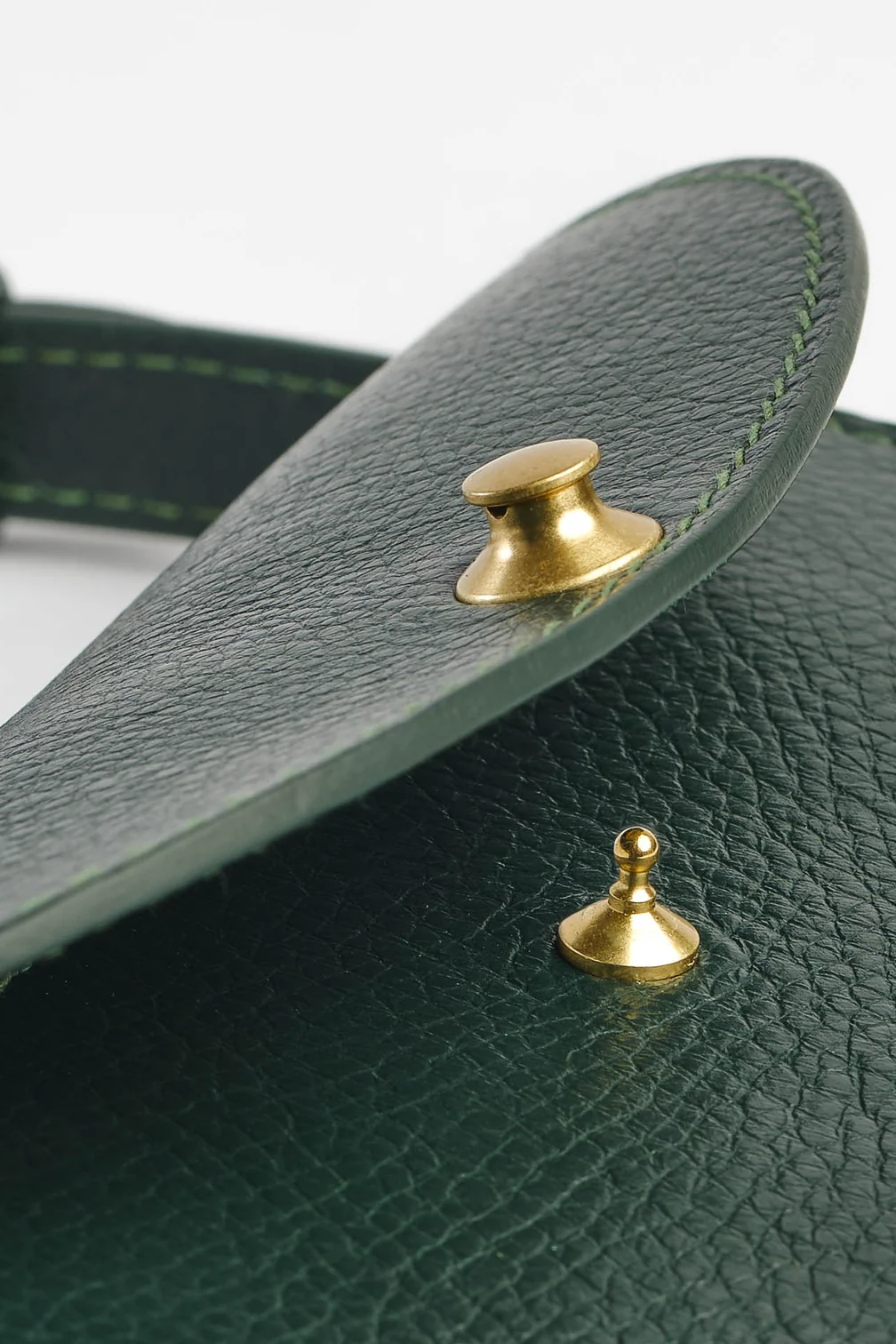 Close-up of a green leather product with gold studs on a white background
