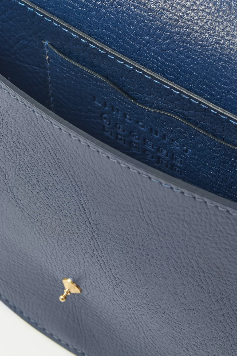 Close-up of a blue leather handbag with a gold logo on a white background