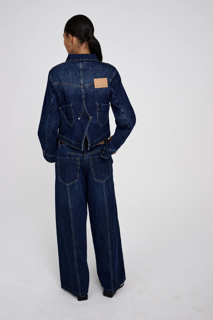 Person wearing a dark blue denim jumpsuit on a white background