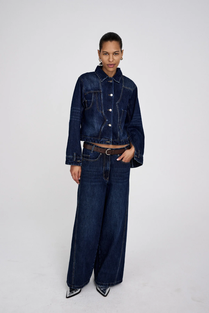 Person wearing a dark blue denim jacket and wide-leg jeans on a white background