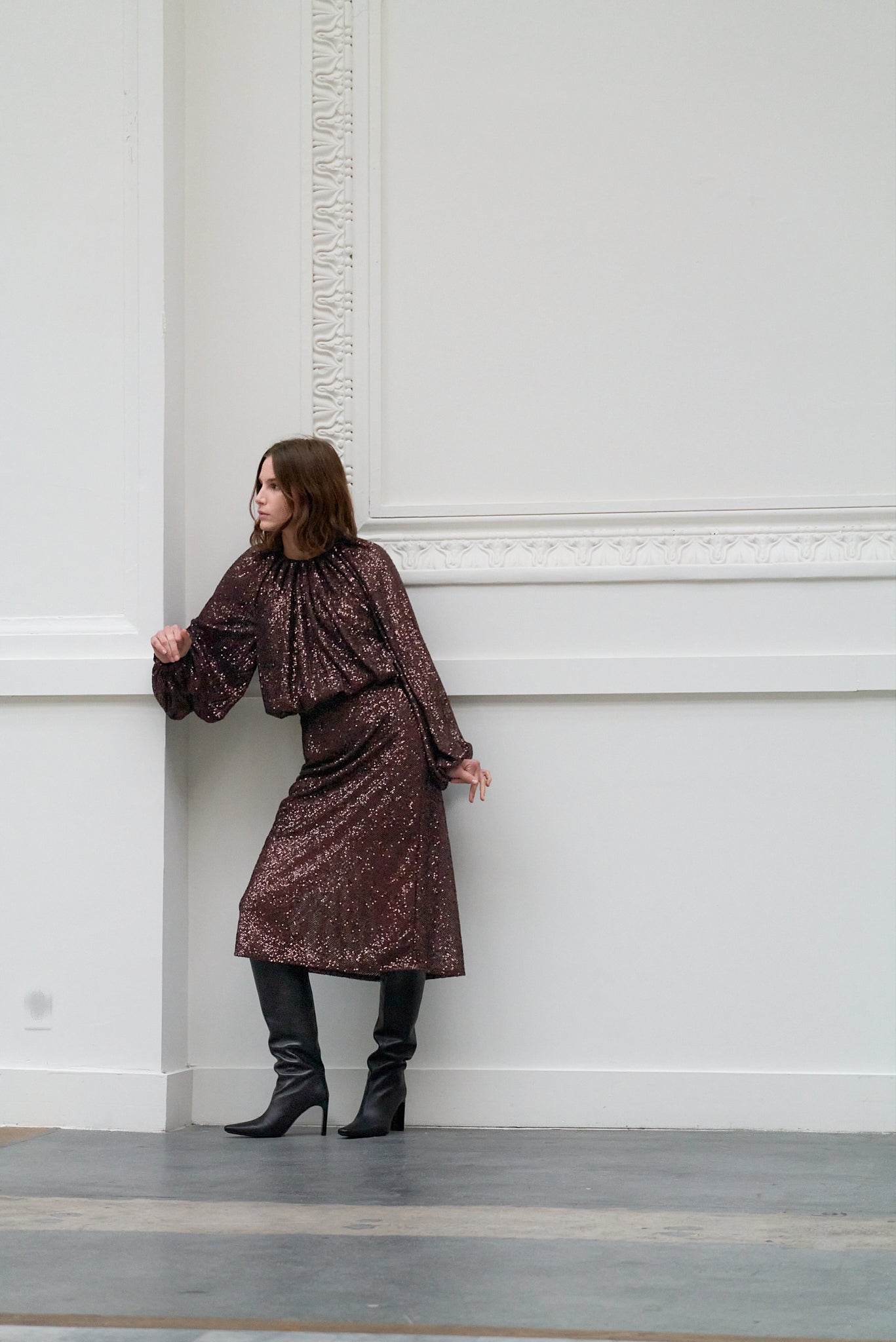 Woman in a brown sequin outfit standing against a white wall