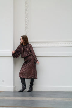 Woman in a brown sequin outfit standing against a white wall