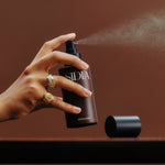 Hand holding a Sidiia spray bottle against a brown background