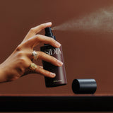 Hand holding a Sidiia spray bottle against a brown background
