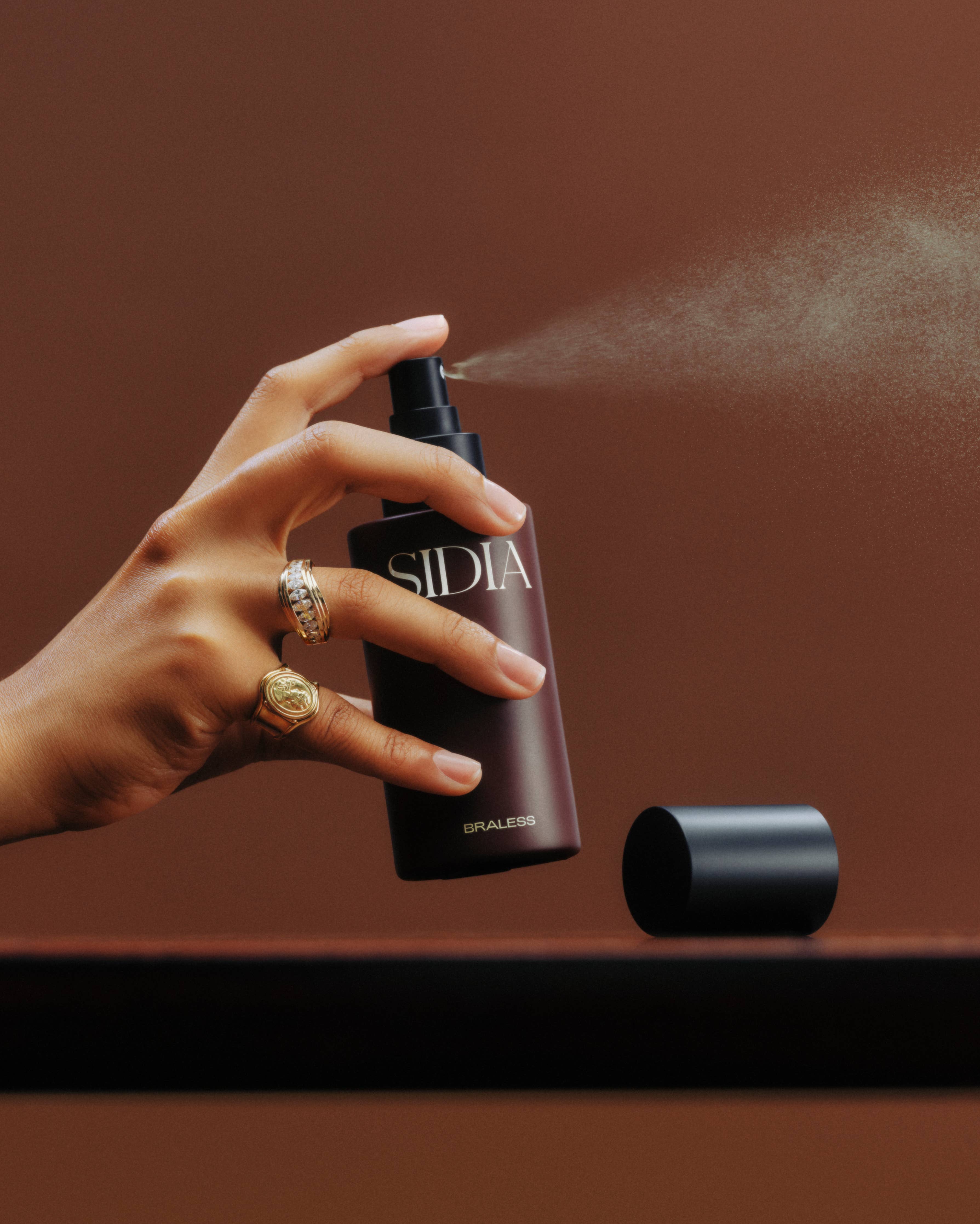 Hand holding a Sidiia spray bottle against a brown background