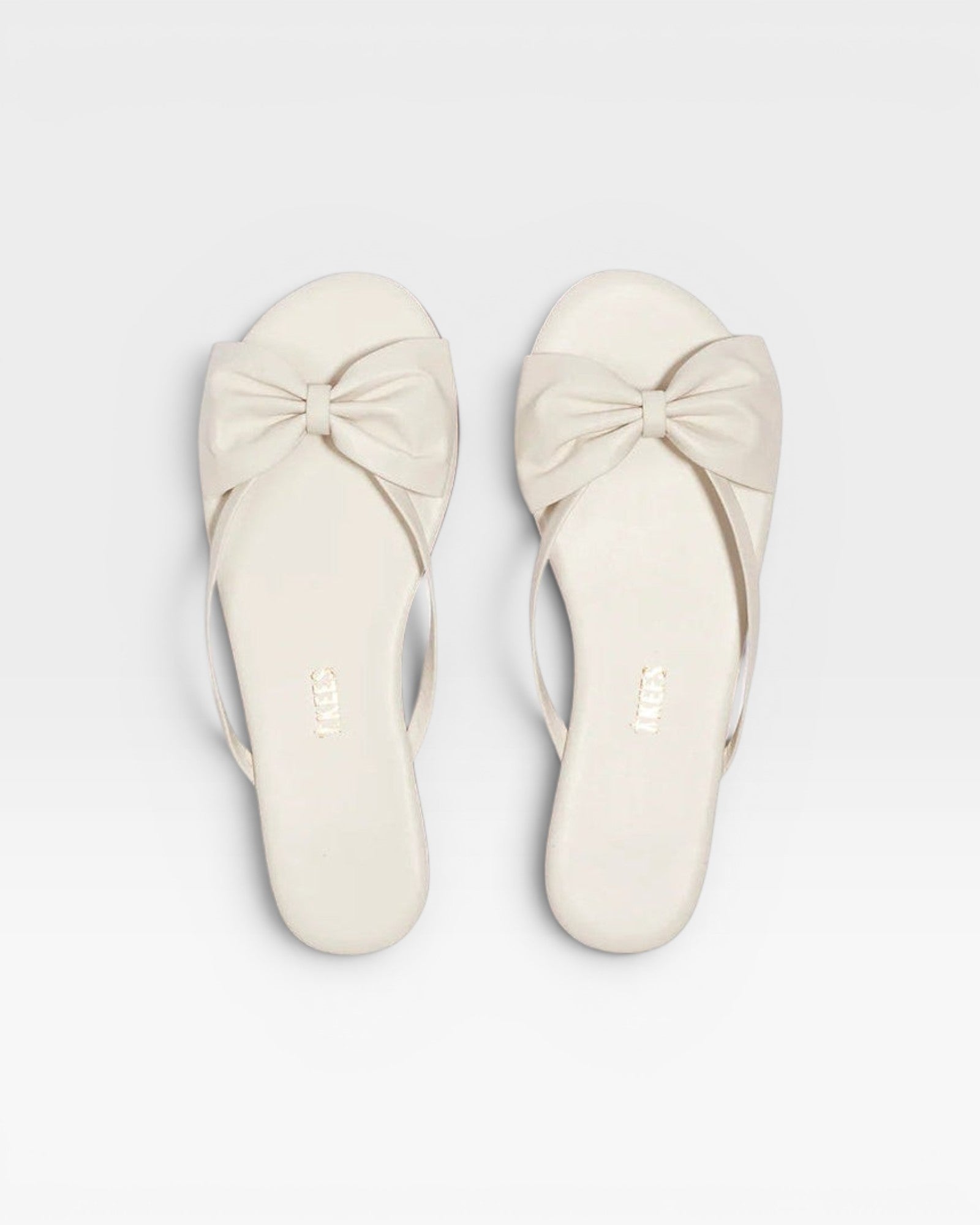 Pair of white sandals with bow details on a white background