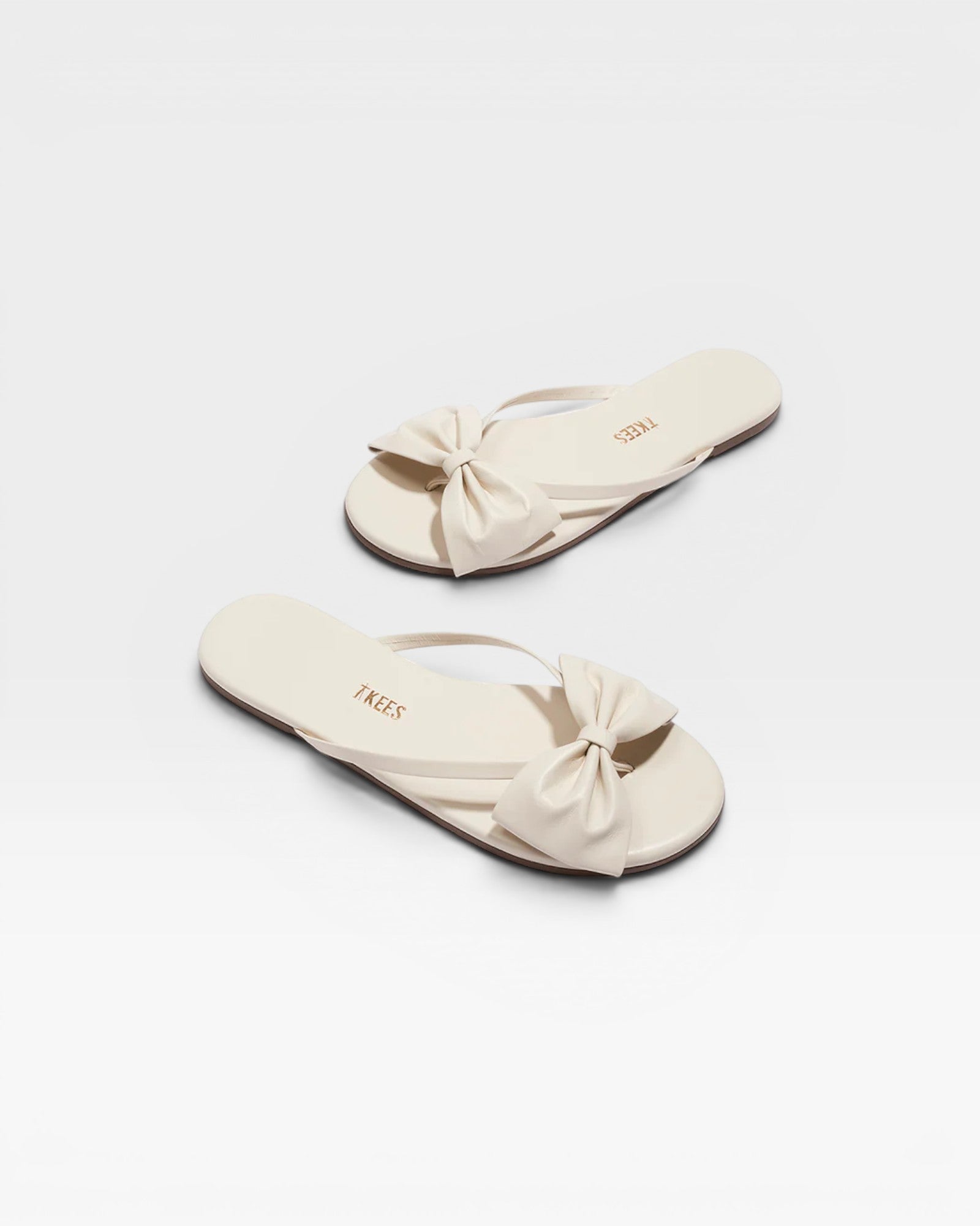 Pair of cream-colored sandals with bow details on a white background