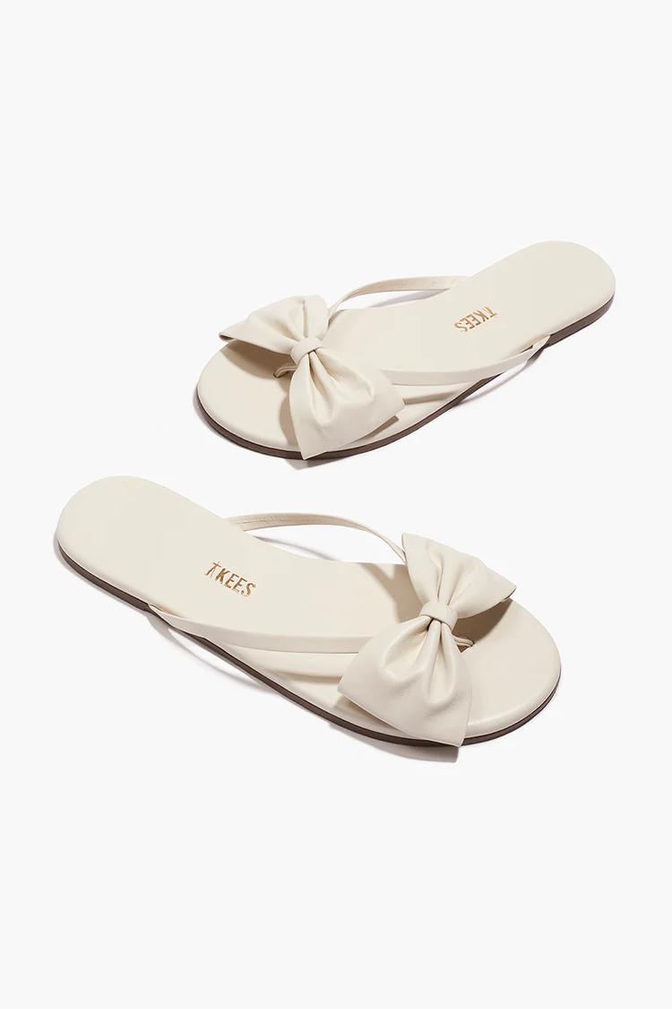 Pair of cream-colored sandals with bow details on a white background