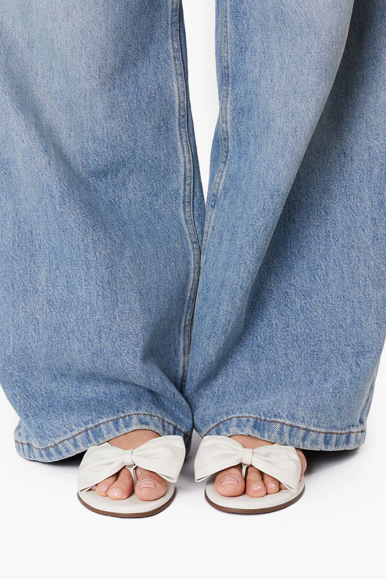 White sandals with bow details worn with blue jeans on a white background