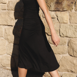 Person wearing a black dress against a stone wall.